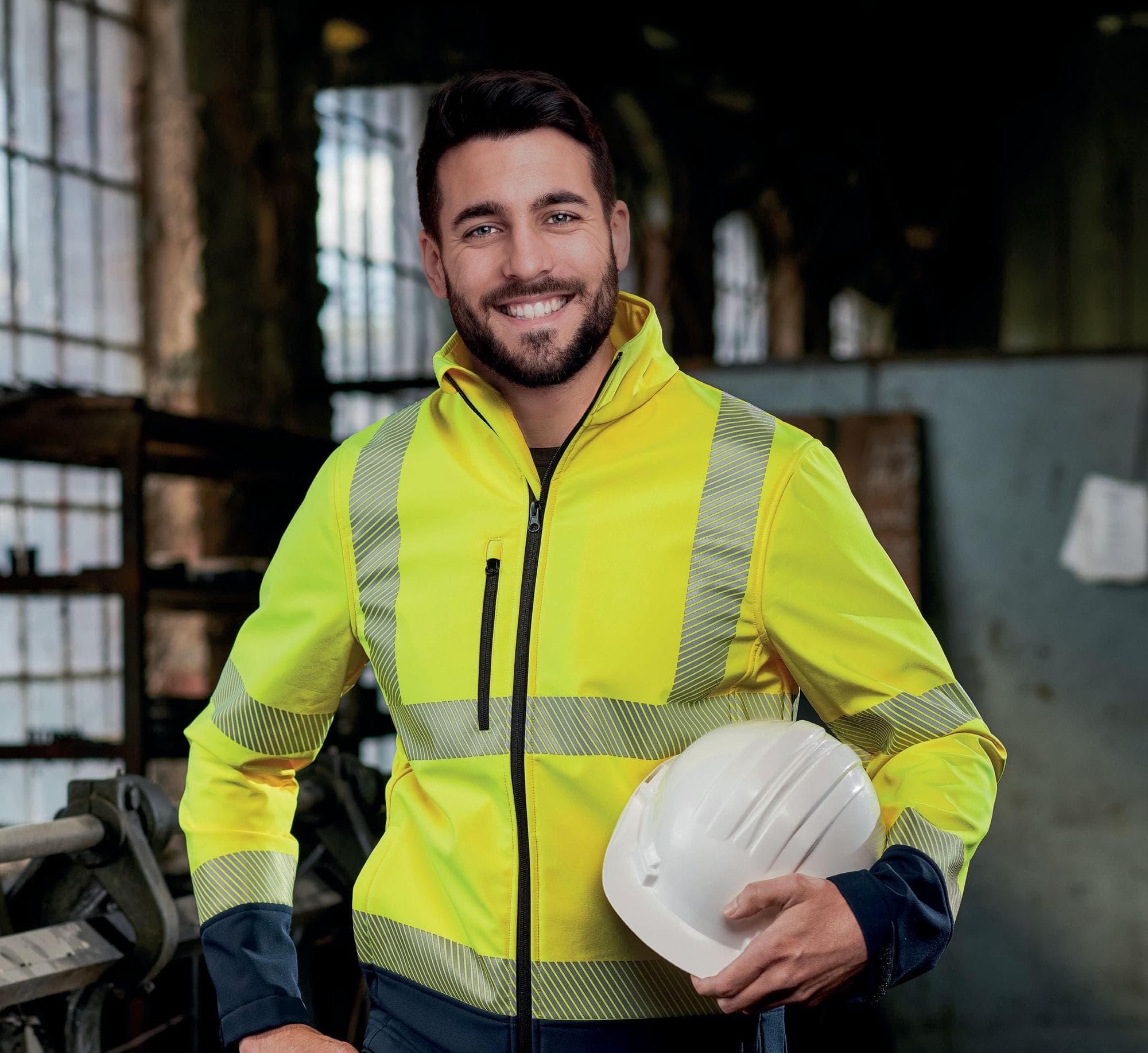 Mitarbeiter in Warnschutz-Softshelljacke mit Schutzhelm in einer Werkstatt